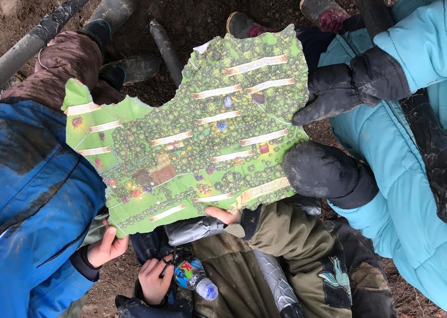 Dzieci w kurtkach i kaloszach, widziane z góry, trzymają razem kolorową mapę terenu